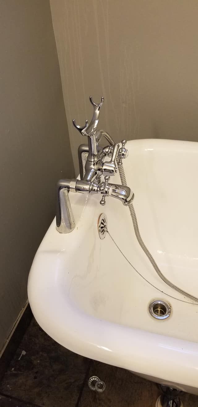 A clawfoot bathtub with ornate chrome faucet and showerhead. The tub is white, with a drain visible.