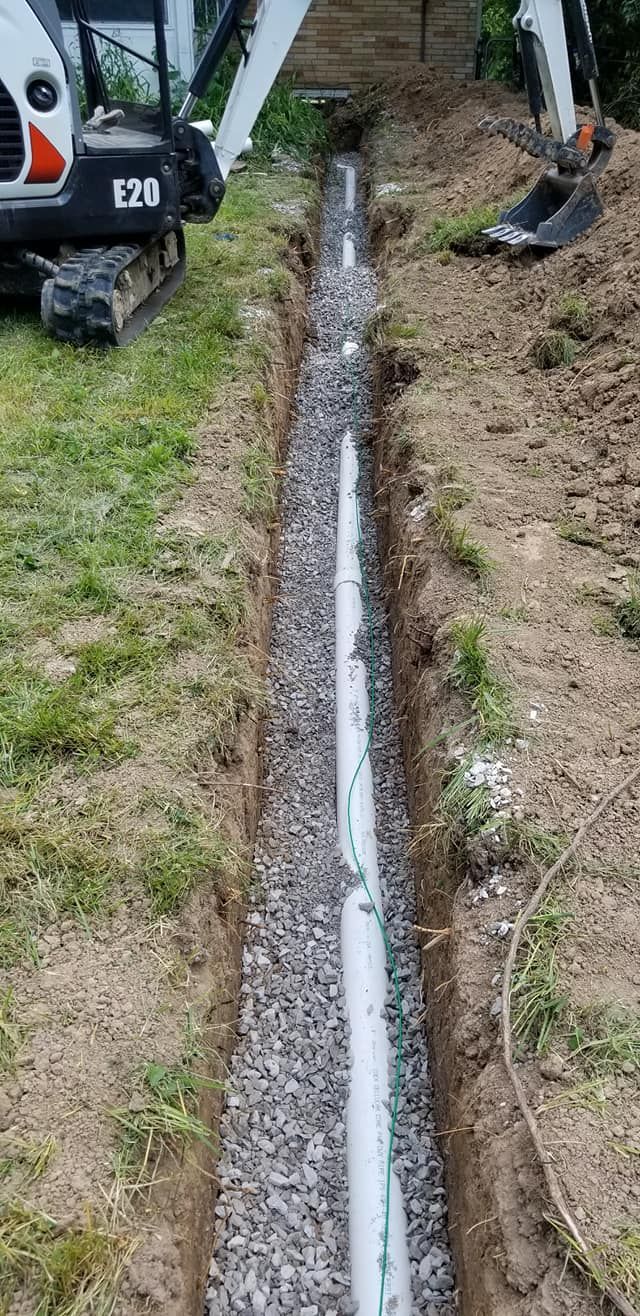 A trench with a pipe installed in gravel, with a small excavator on the left and right.