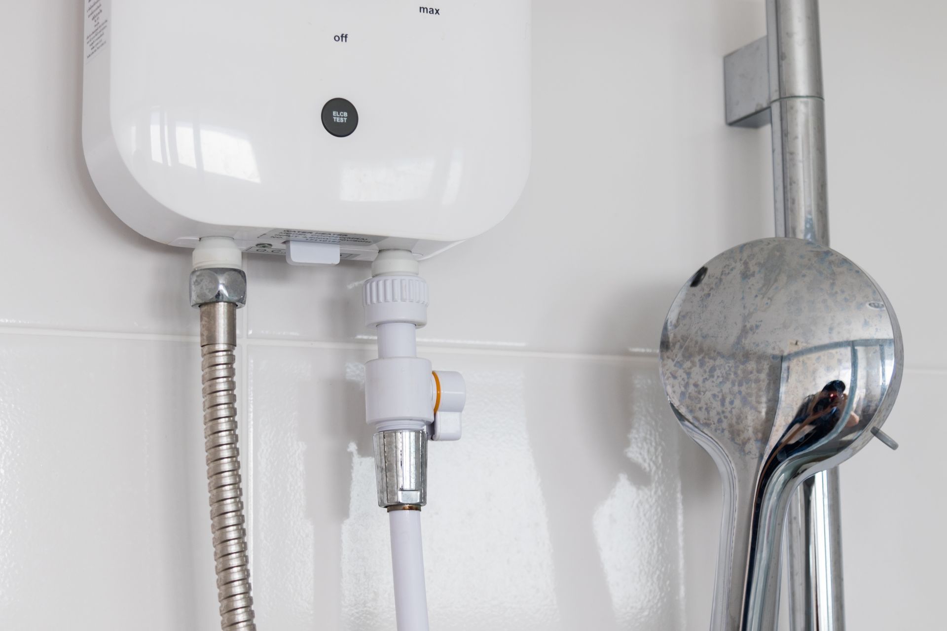 White electric water heater mounted on white tiled wall near a shower head.