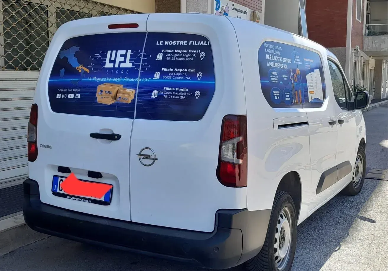 Furgone bianco con pannelli pubblicitari blu parcheggiato in strada.