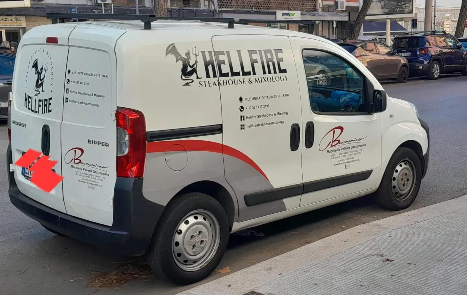 Furgone Hellfire bianco parcheggiato in strada, vista posteriore laterale con decalcomanie rosse e nere.