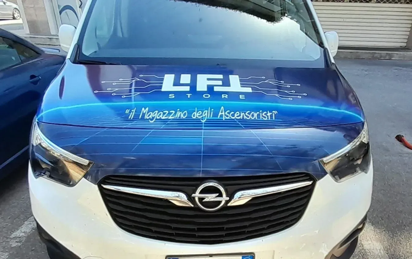 Un'auto Opel blu e bianca con il logo aziendale sul cofano, parcheggiata all'aperto.