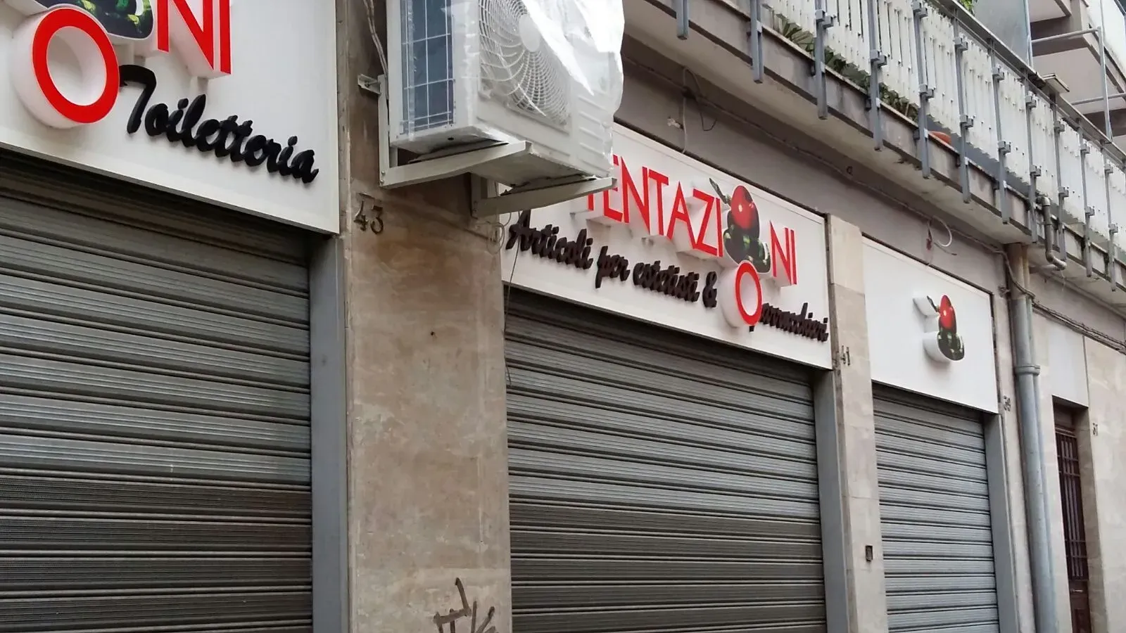 Vetrine chiuse con serrande grigie e insegne bianche all'angolo di una strada cittadina