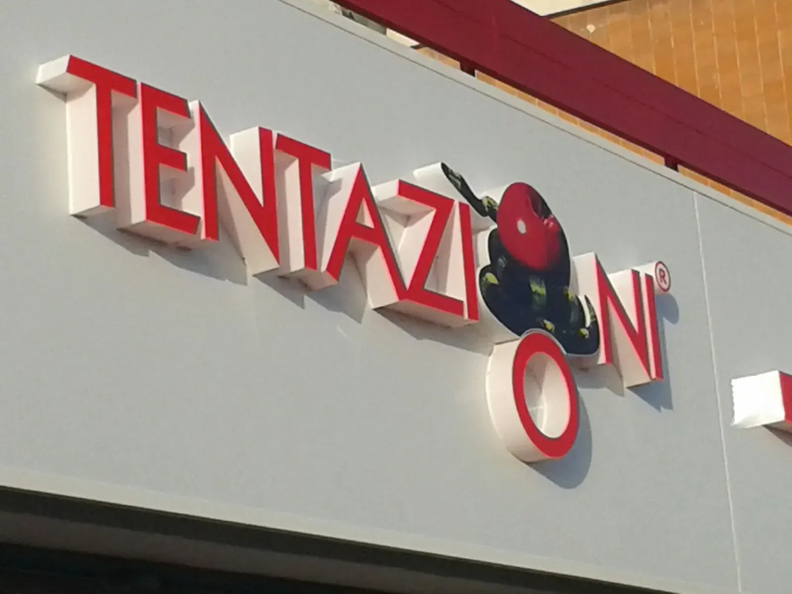 Insegna di Tentazione in lettere rosse con il logo di una coccinella sulla facciata del negozio.