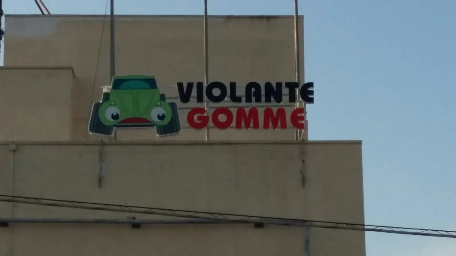 Insegna di Violante Gomme con il logo di un'auto verde sulla facciata beige di un edificio.