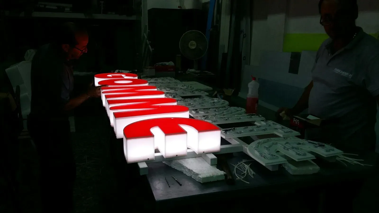 File di articoli confezionati in rosso e bianco disposti su un tavolo in un ambiente interno poco illuminato.