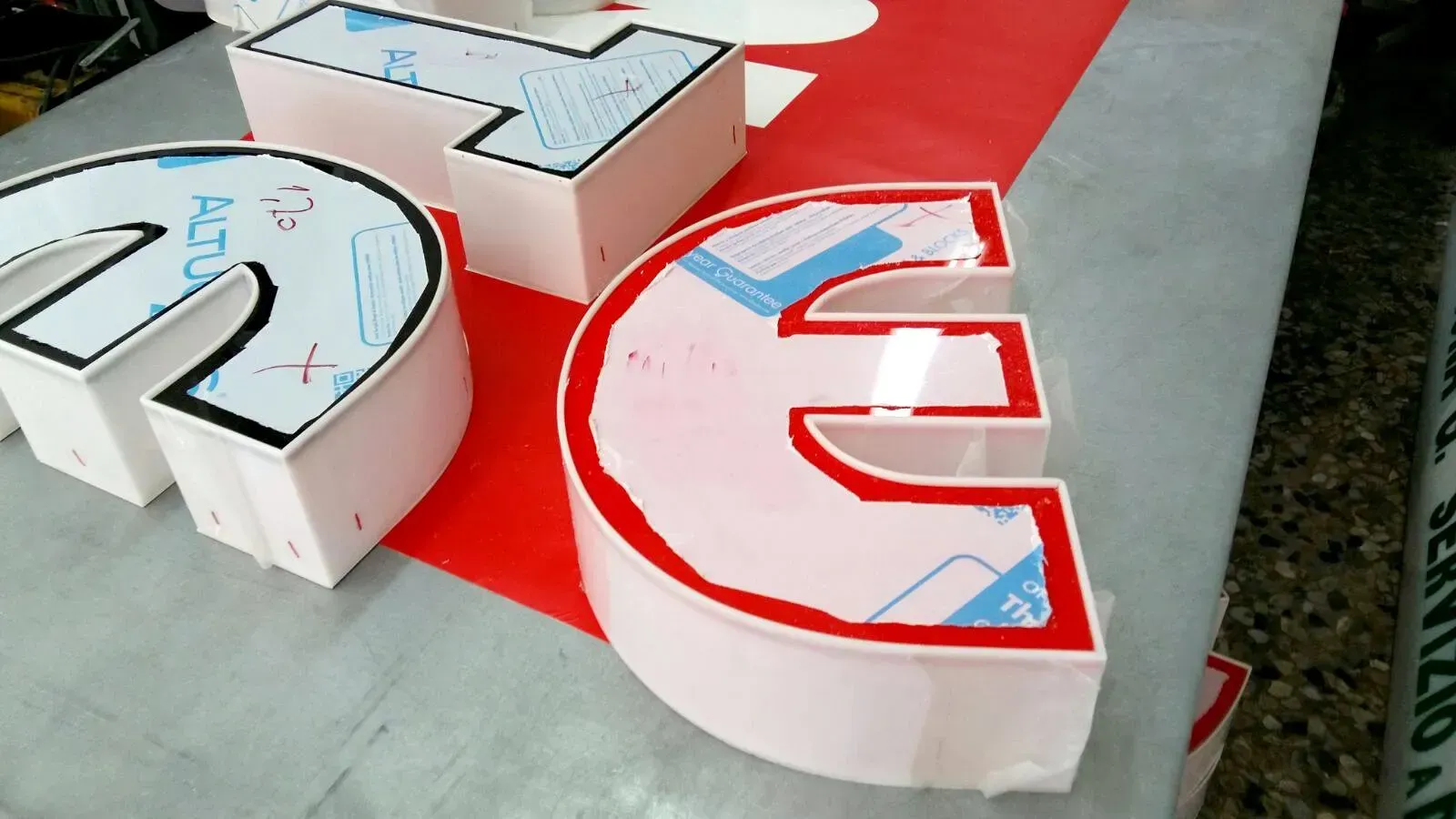 Lettere 3D bianche con dettagli blu su una superficie rossa e grigia, viste dall'alto.