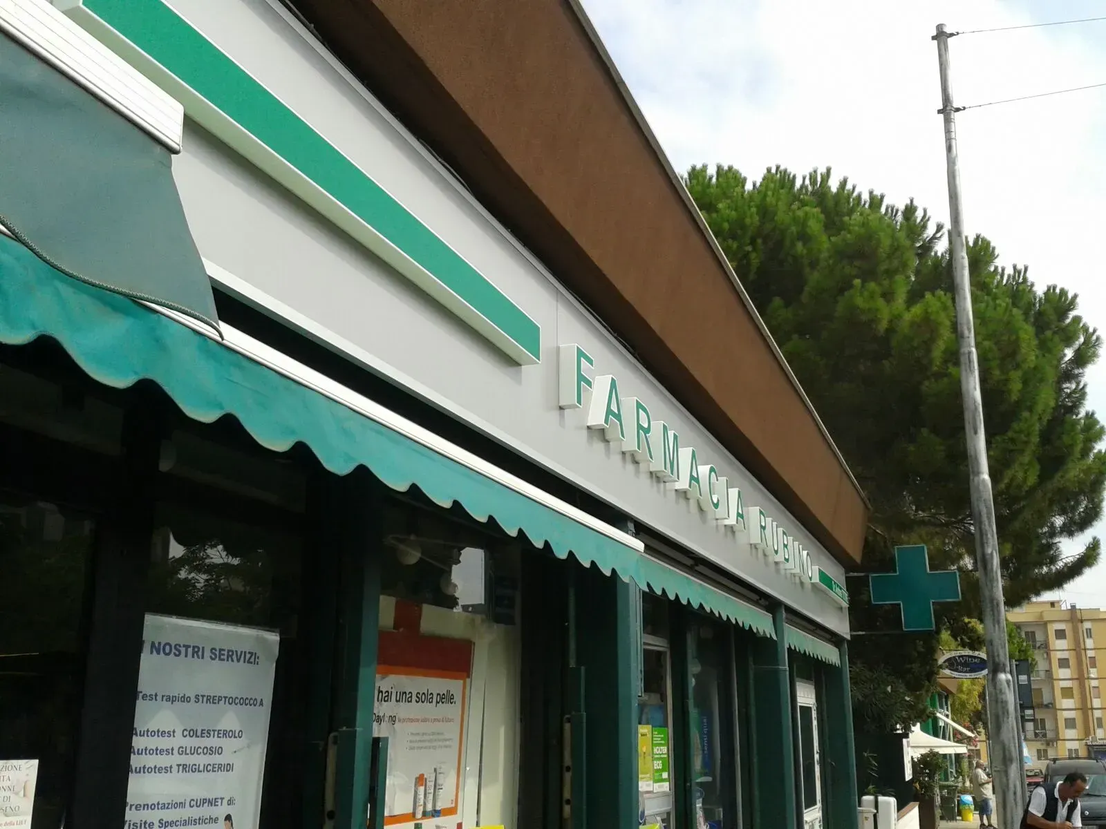 Negozio d'angolo con tenda da sole verde e insegna su una via cittadina