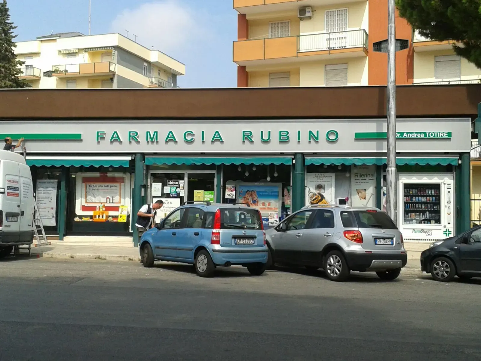 Vista stradale della facciata della Farmacia Rubino con auto parcheggiate davanti.