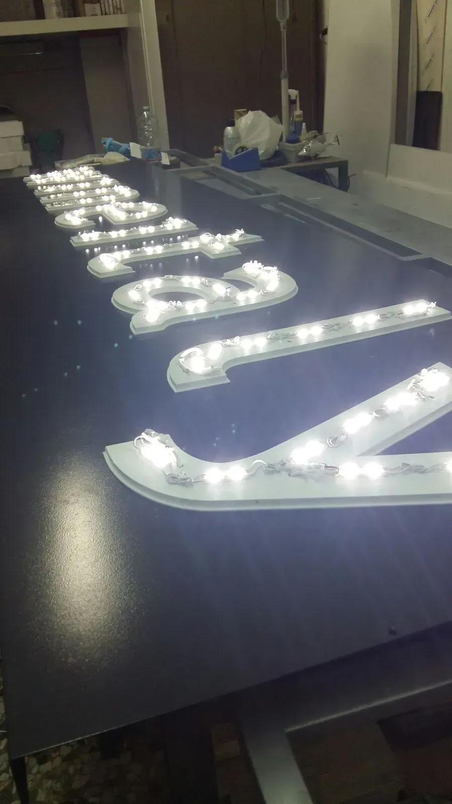 Lettere luminose bianche su un piano di tavolo scuro in un'officina o in una stanza per la realizzazione di insegne.