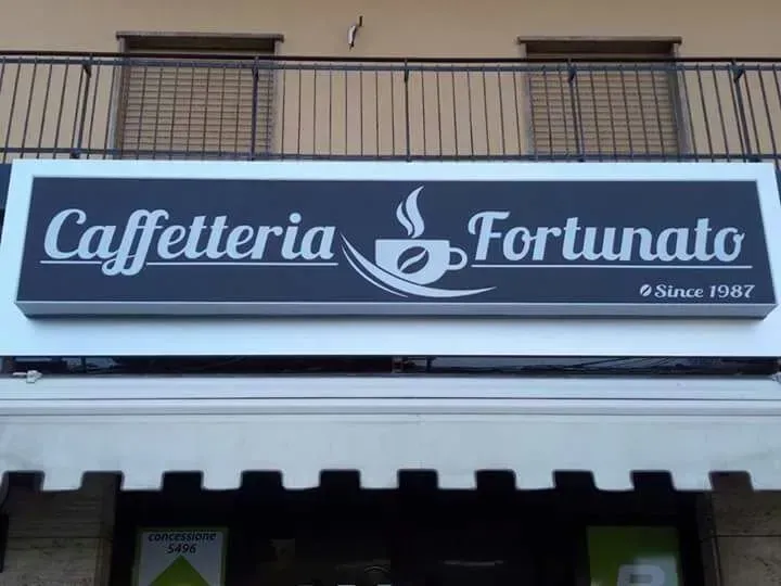 Insegna della Caffetteria Fortunato in scritta bianca su tenda da sole blu scuro, con il logo di una tazza di caffè.