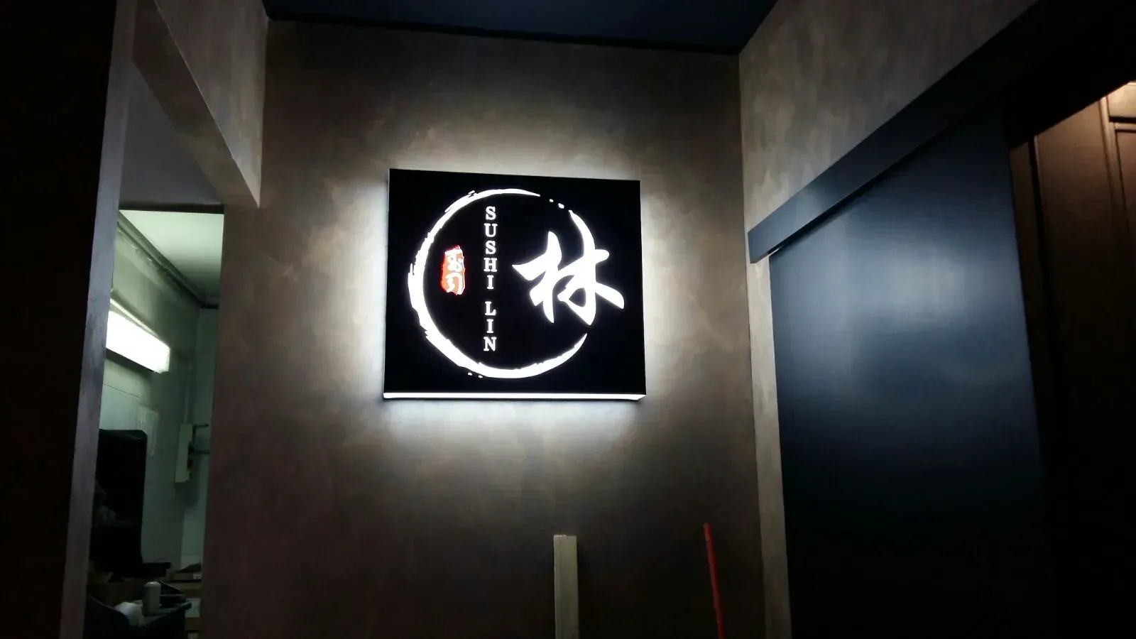 Insegna nera retroilluminata con caratteri giapponesi bianchi su una parete del corridoio