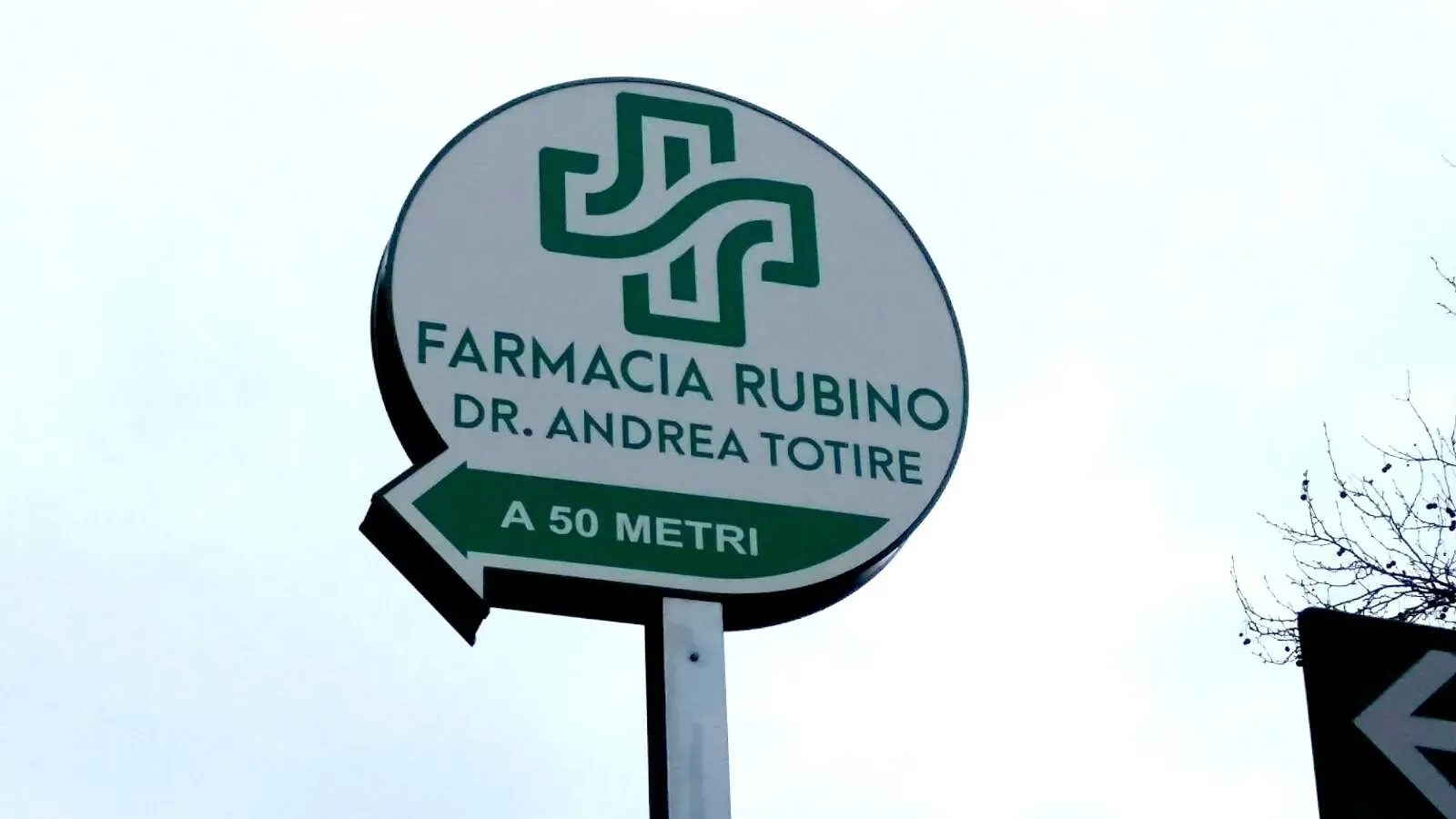 Insegna della farmacia con la scritta “Farmacia Rubino Dr. Andrea Totire” con freccia e “A 50 metri” in verde e bianco