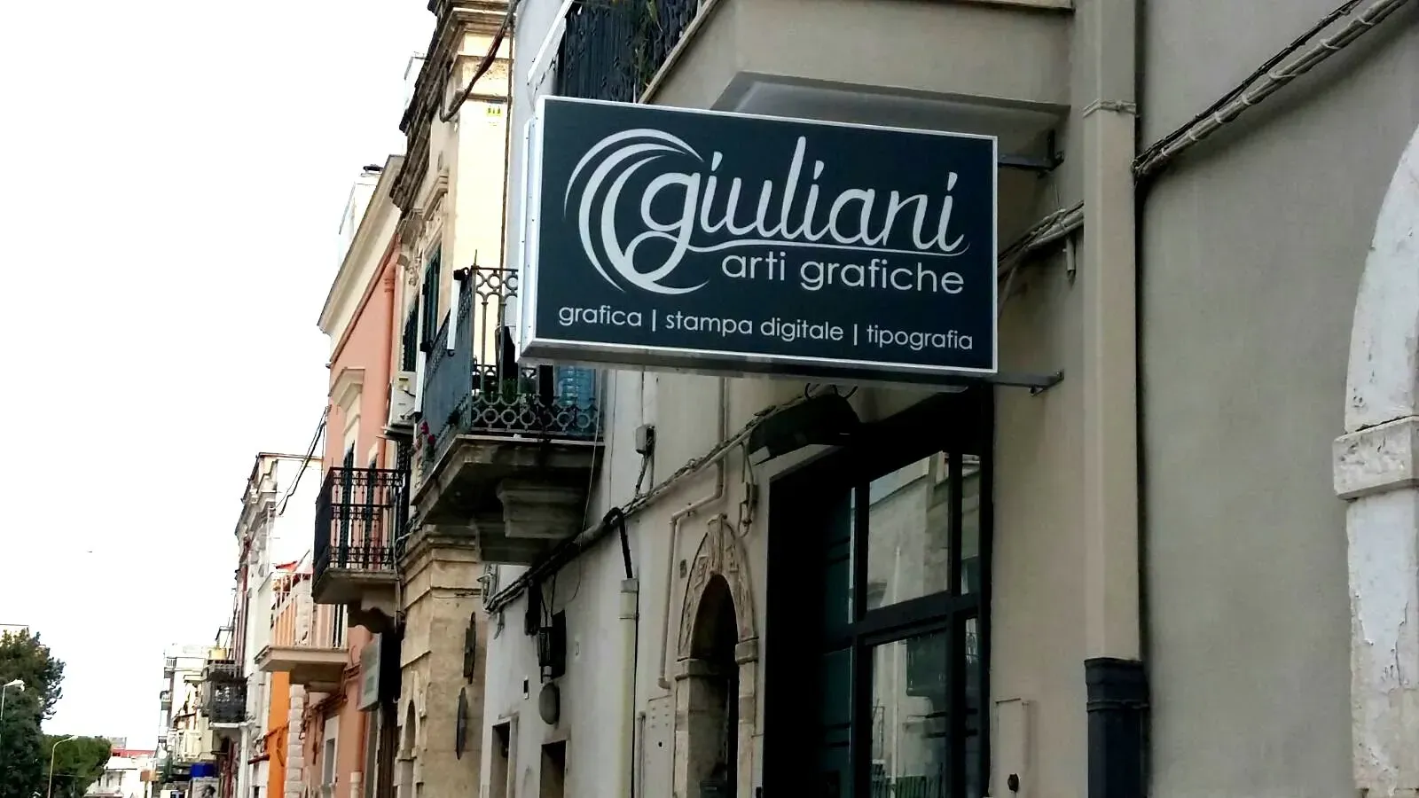 Insegna del negozio “Giuliani arti grafiche” su una via stretta, con edifici e balconi nelle vicinanze