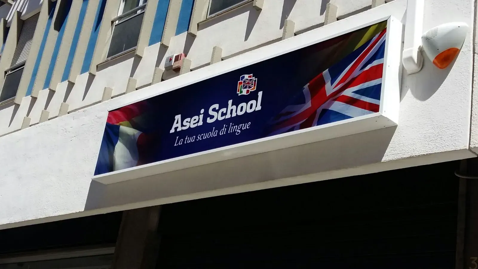 Cartello della Asel School con la bandiera del Regno Unito sulla facciata bianca dell'edificio.