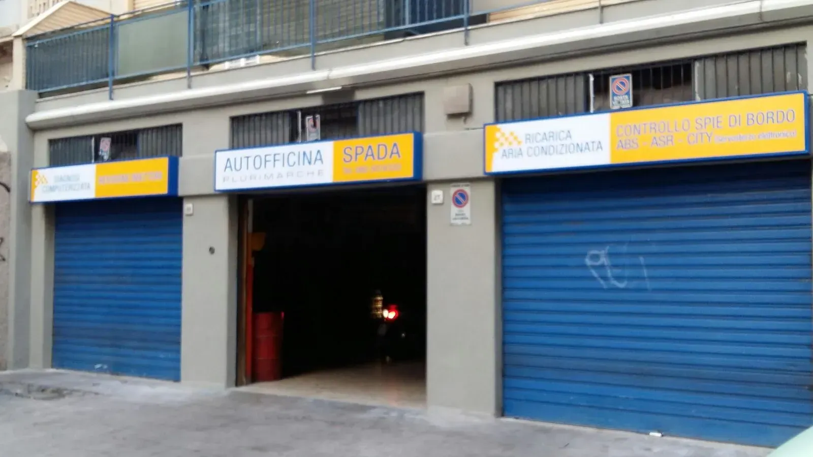 Porte avvolgibili blu sulla facciata di un'officina meccanica, con un'auto visibile all'interno dell'ingresso centrale aperto del garage.
