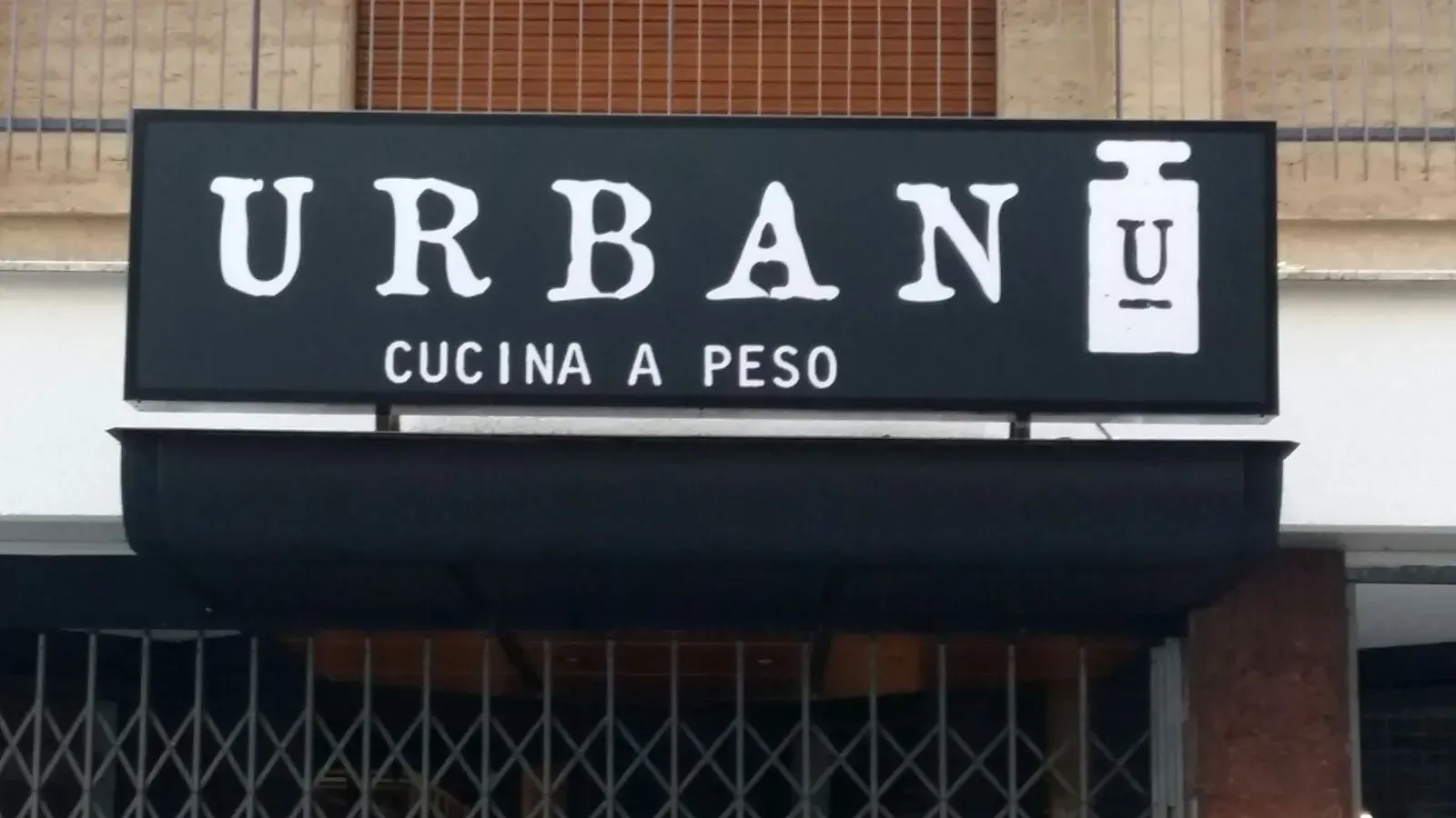 Insegna del ristorante URBAN Cucina a Peso su una tenda da sole nera sulla vetrina.