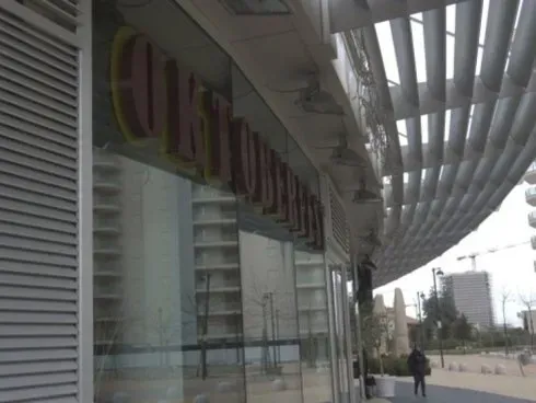 Vetrina moderna e passaggio pedonale coperto lungo una via cittadina, con alcuni pedoni in lontananza.