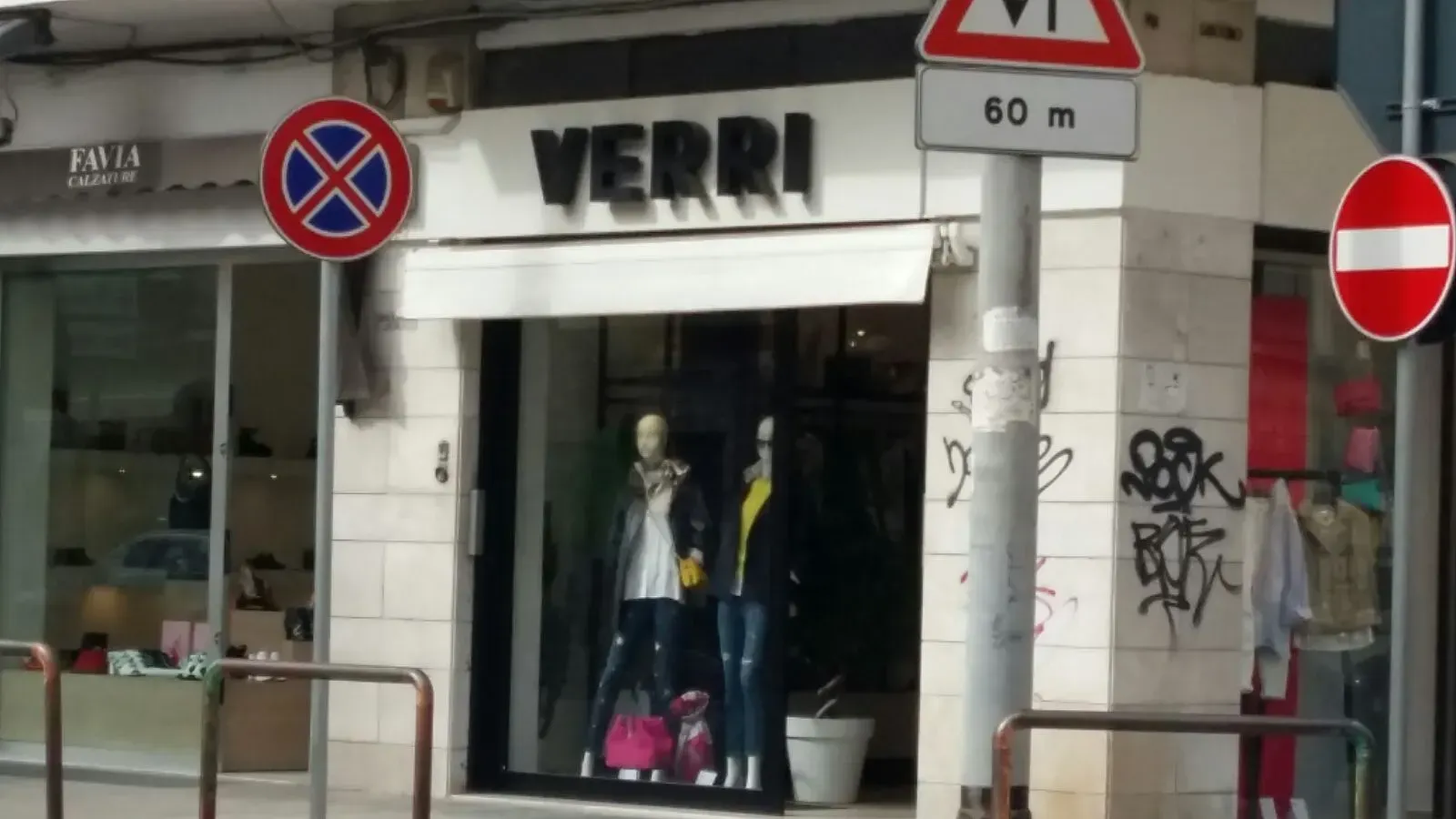 Ingresso di un negozio di abbigliamento con manichini e cartelli di saldi su una via cittadina.