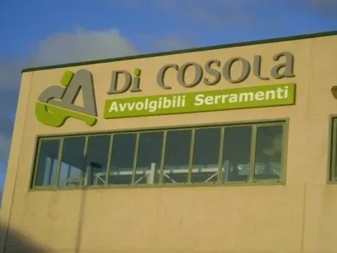 Di Cosola Avvolgibili Serramenti sign on a beige building with windows against a blue sky