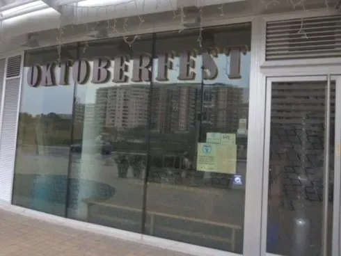 Vetrina con la scritta “OKTOBERFEST” e riflessi degli edifici circostanti.