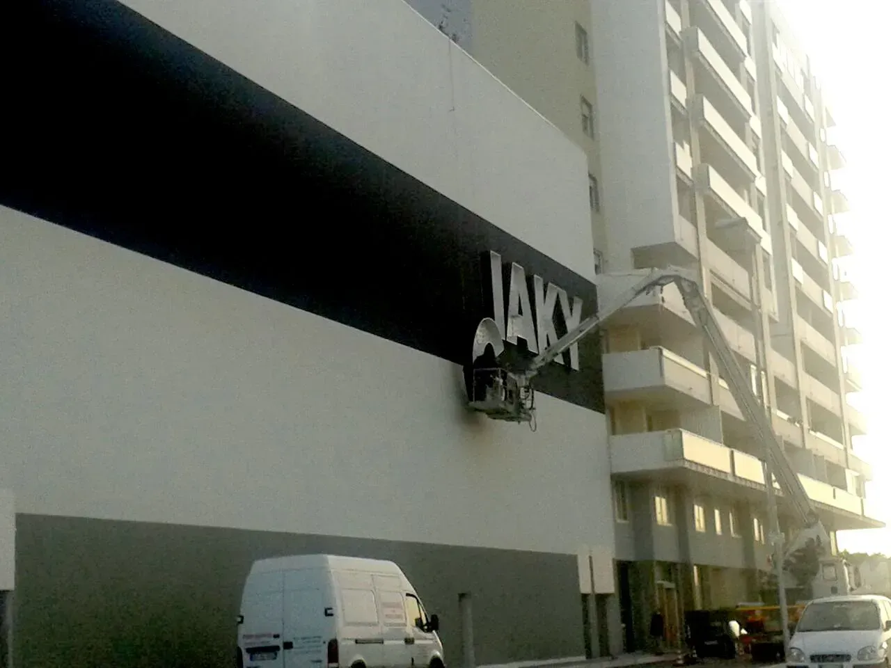 Esterno di un grattacielo con un furgone bianco parcheggiato al piano inferiore e un'insegna appesa al muro.
