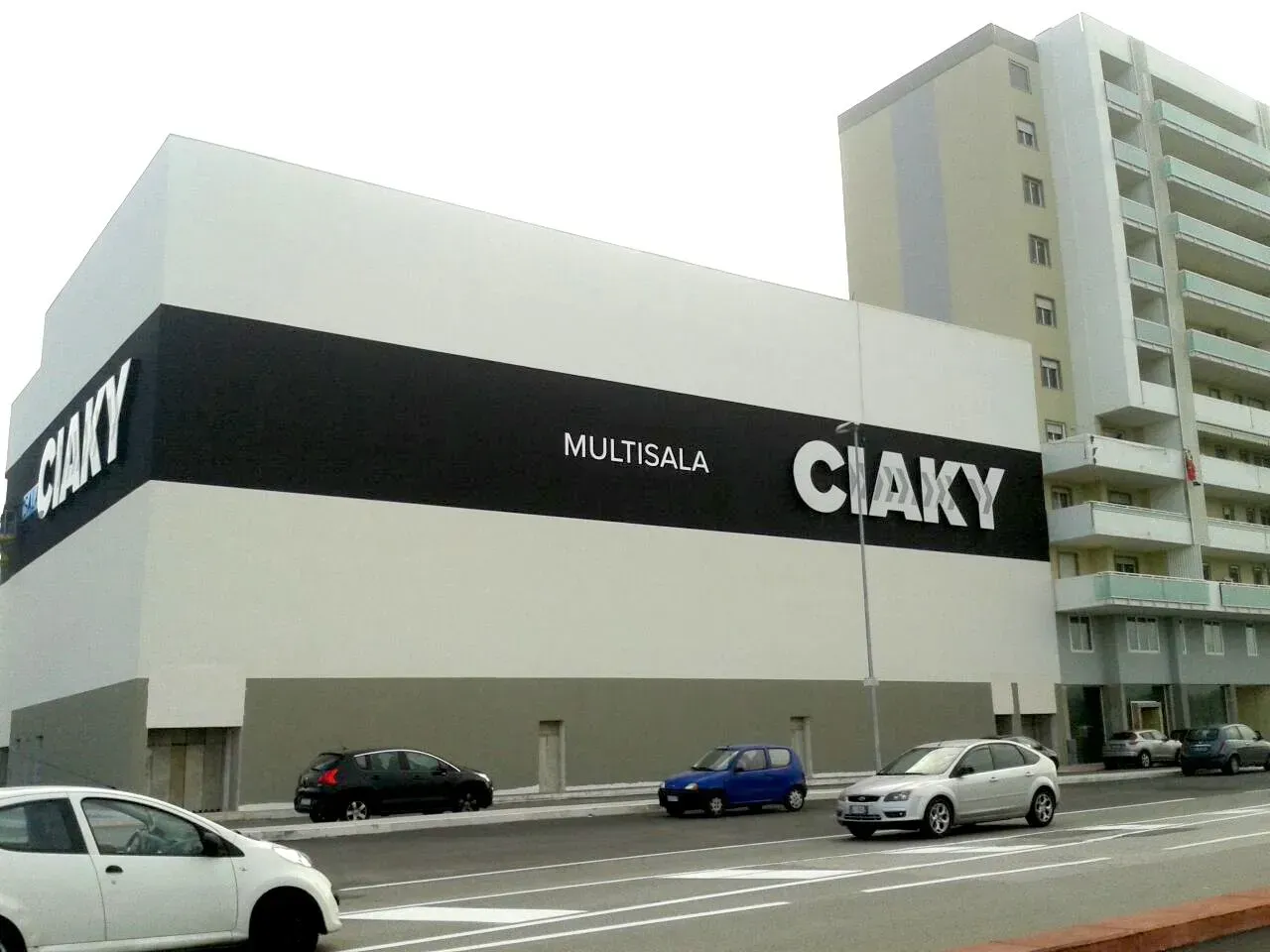 Grande edificio della CIAY con insegna nera su una strada cittadina, con auto parcheggiate davanti.