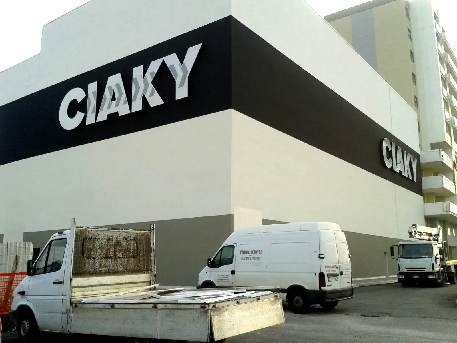 Esterno del magazzino CIAKY con furgoni per le consegne parcheggiati all'esterno e una grande insegna in bianco e nero.