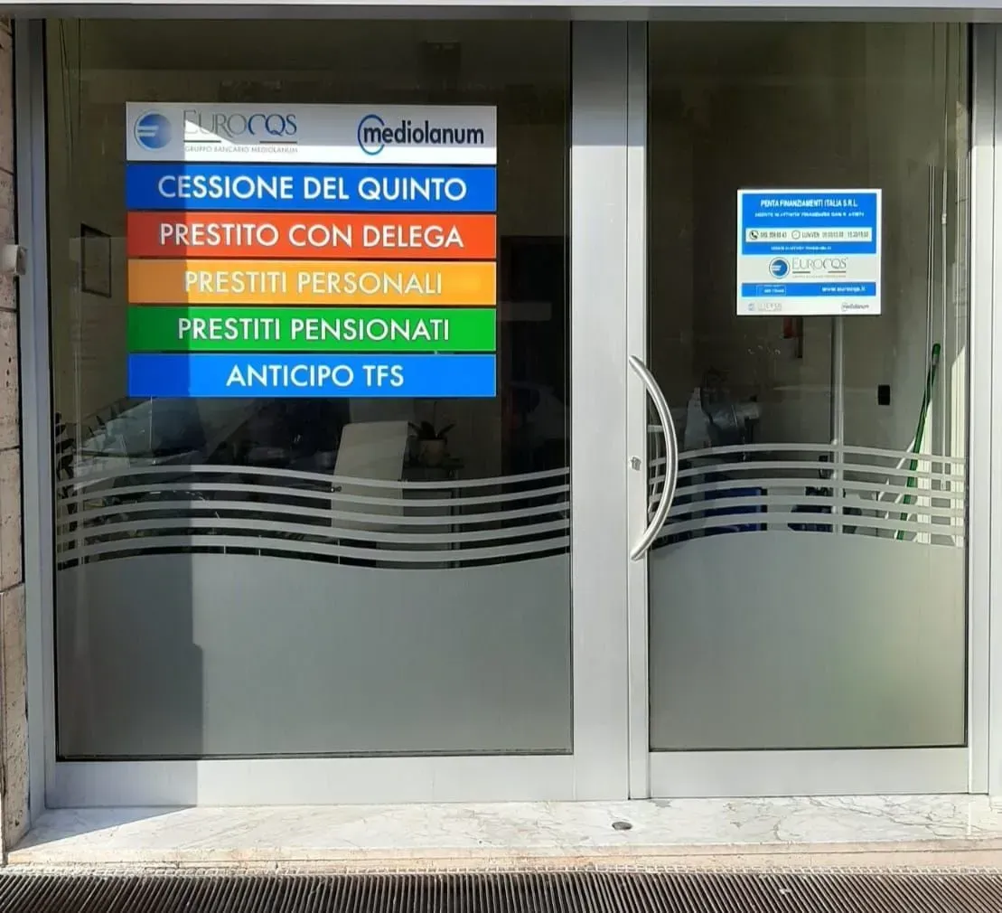 Vetrina con insegne di servizi di prestito italiani nei colori blu, arancione, verde e rosso su ante satinate.