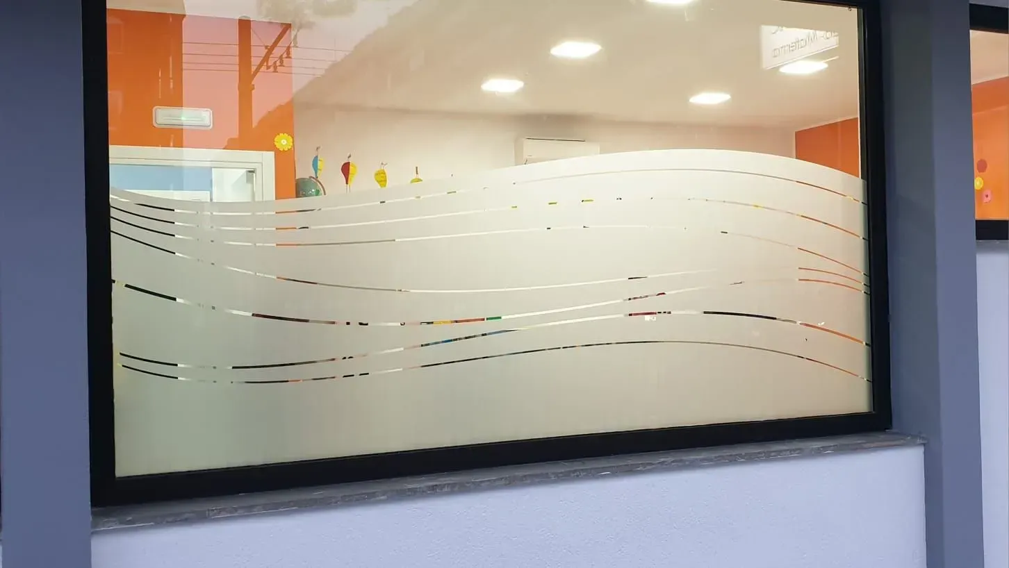 Finestra da ufficio in vetro satinato con linee ondulate incise e luci interne calde alle sue spalle.