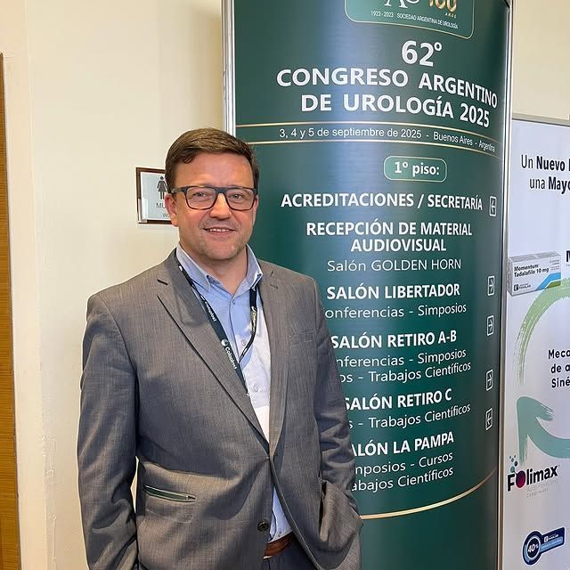 Hombre con traje gris de pie junto a un cartel de la conferencia en el 62º Congreso Argentino de Urología.