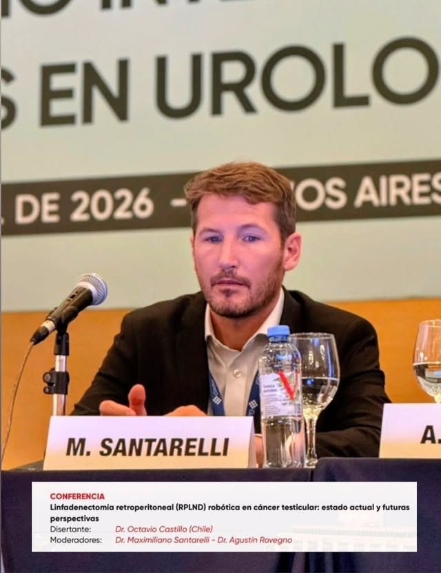 Un hombre hablando en una mesa de conferencias con micrófonos y una placa con el nombre