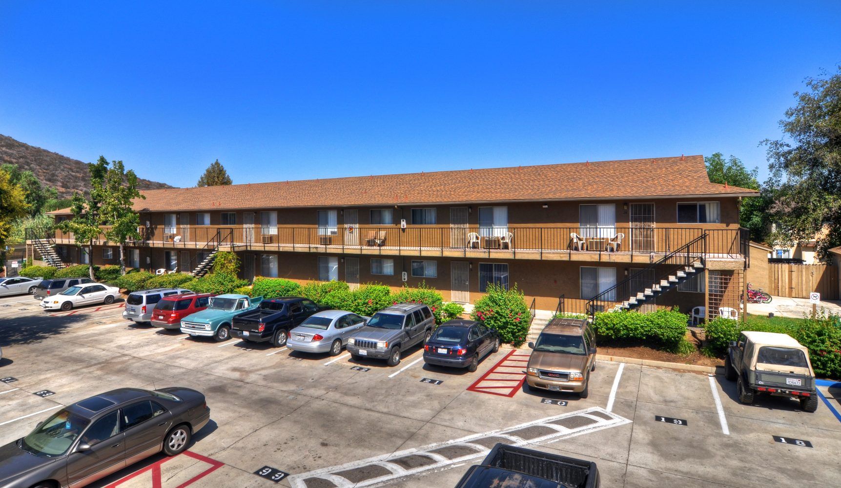 Motel-style two-story building with red roof and parked cars in front on a sunny day