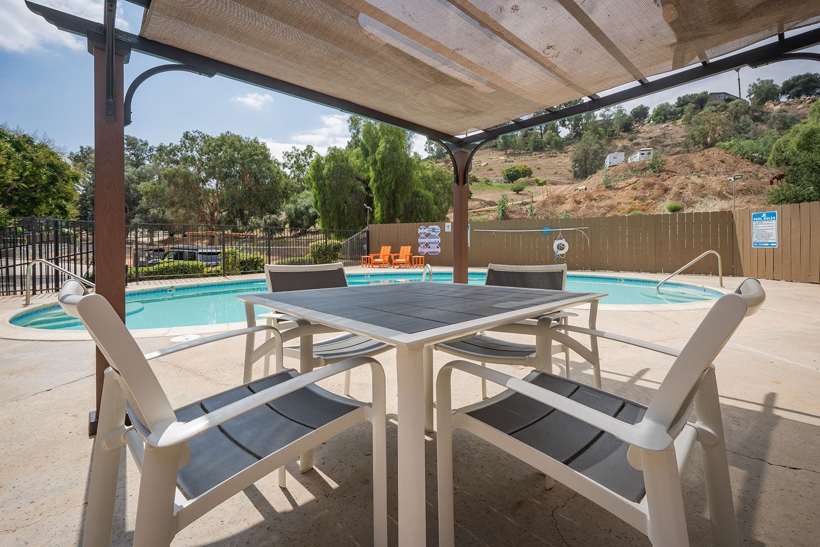 Patio table and chairs under a pergola beside an outdoor swimming pool on a sunny day