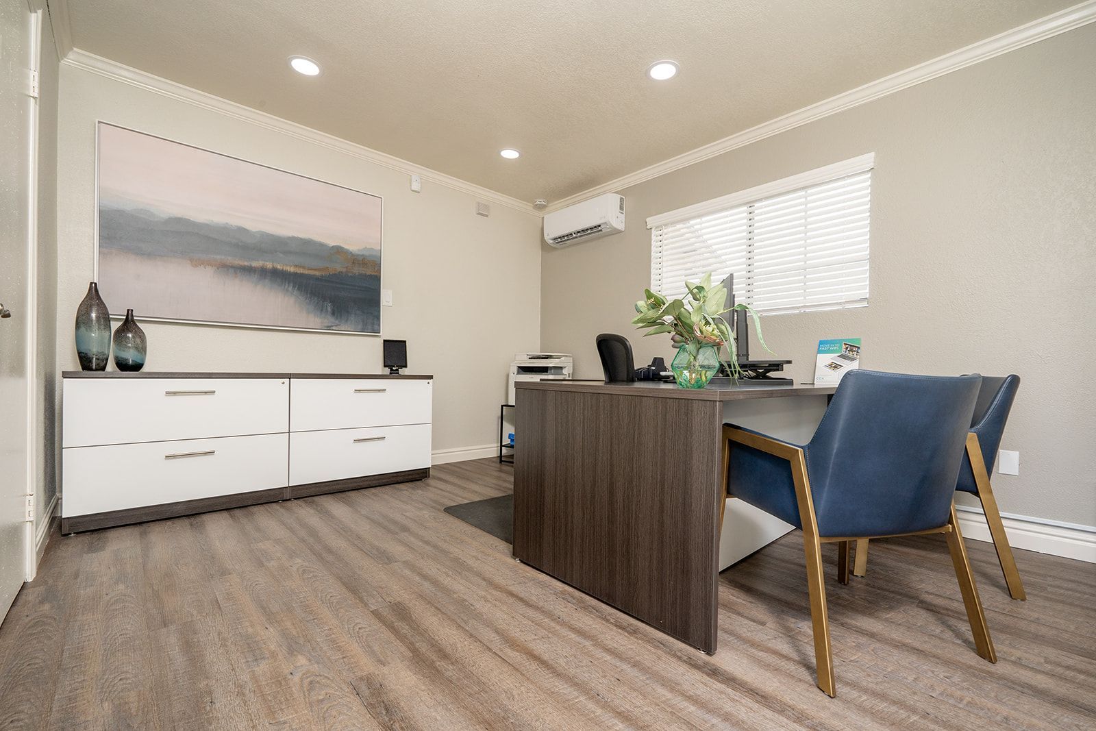 Modern living room with white sideboard, dark desk, blue chairs, and large abstract wall art