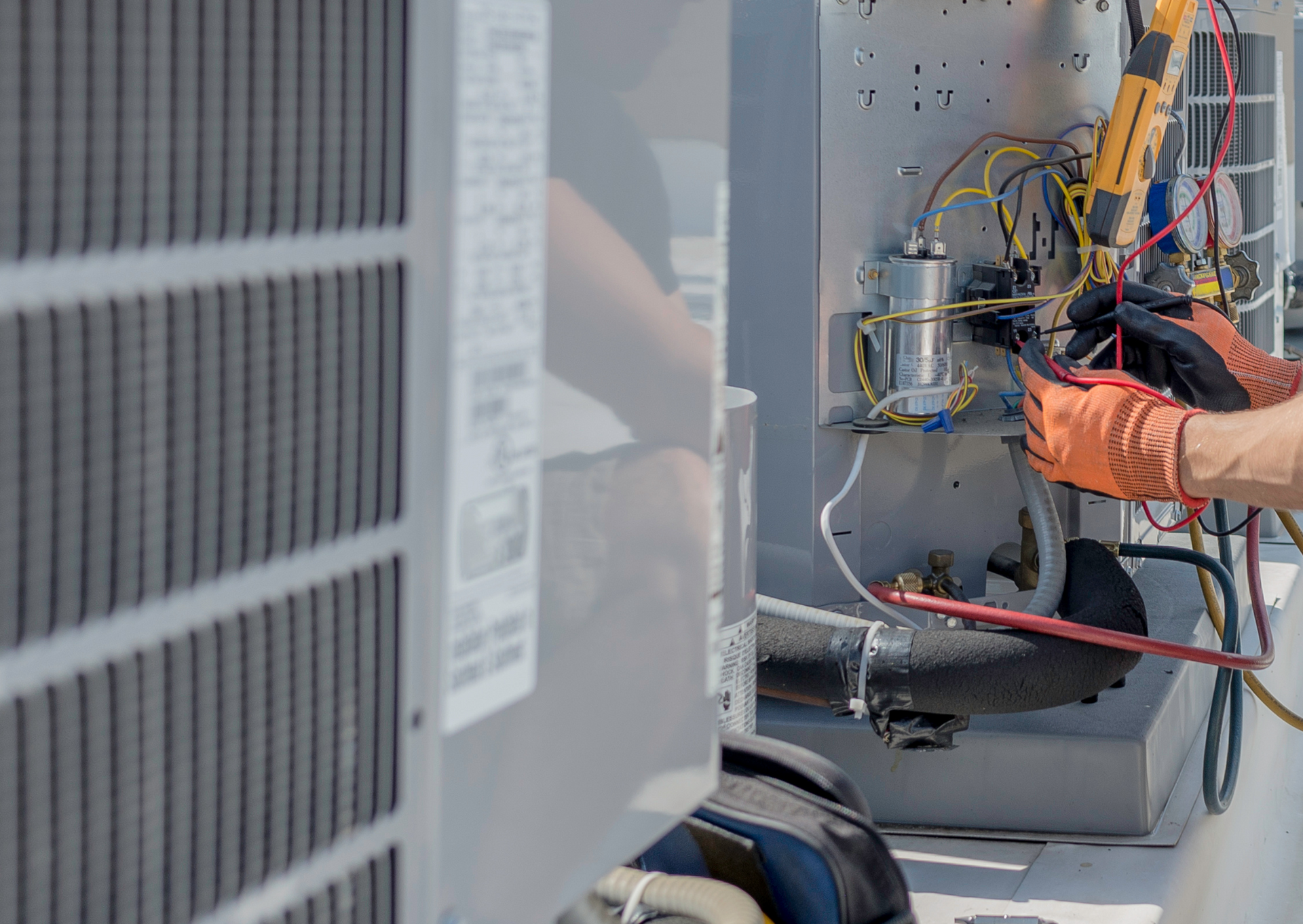 HVAC technician repairing an air conditioning unit on a rooftop. Orange gloves, wires, tools visible.