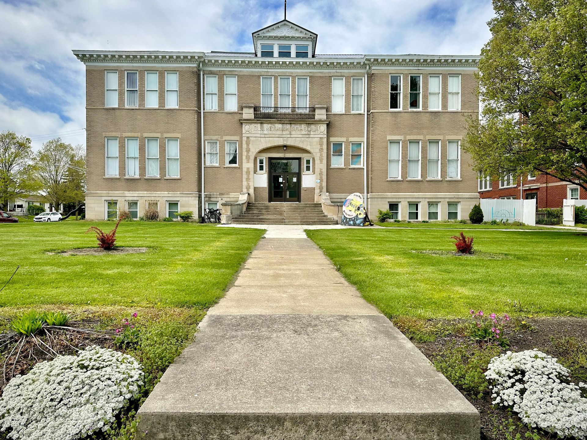 Blume High School, with a red roof is sitting on top of a lush green field.