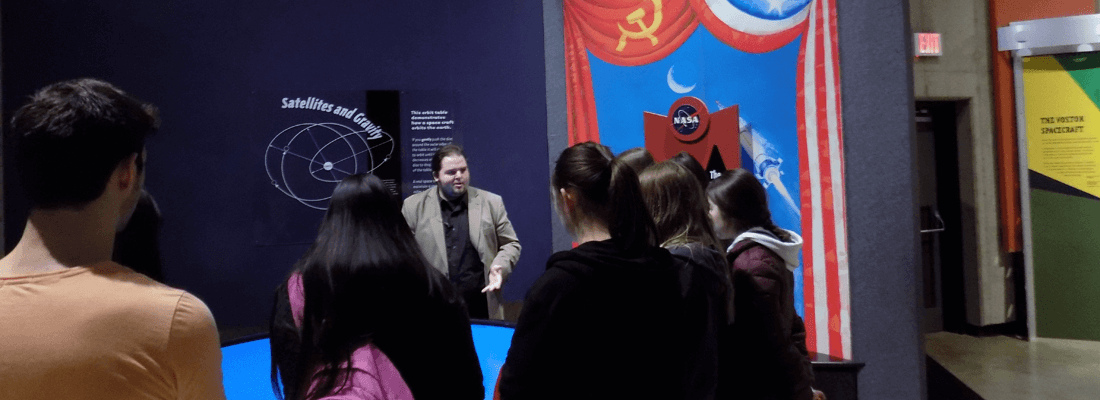 A group of people are gathered during a tour to listen about orbiting around Earth.
