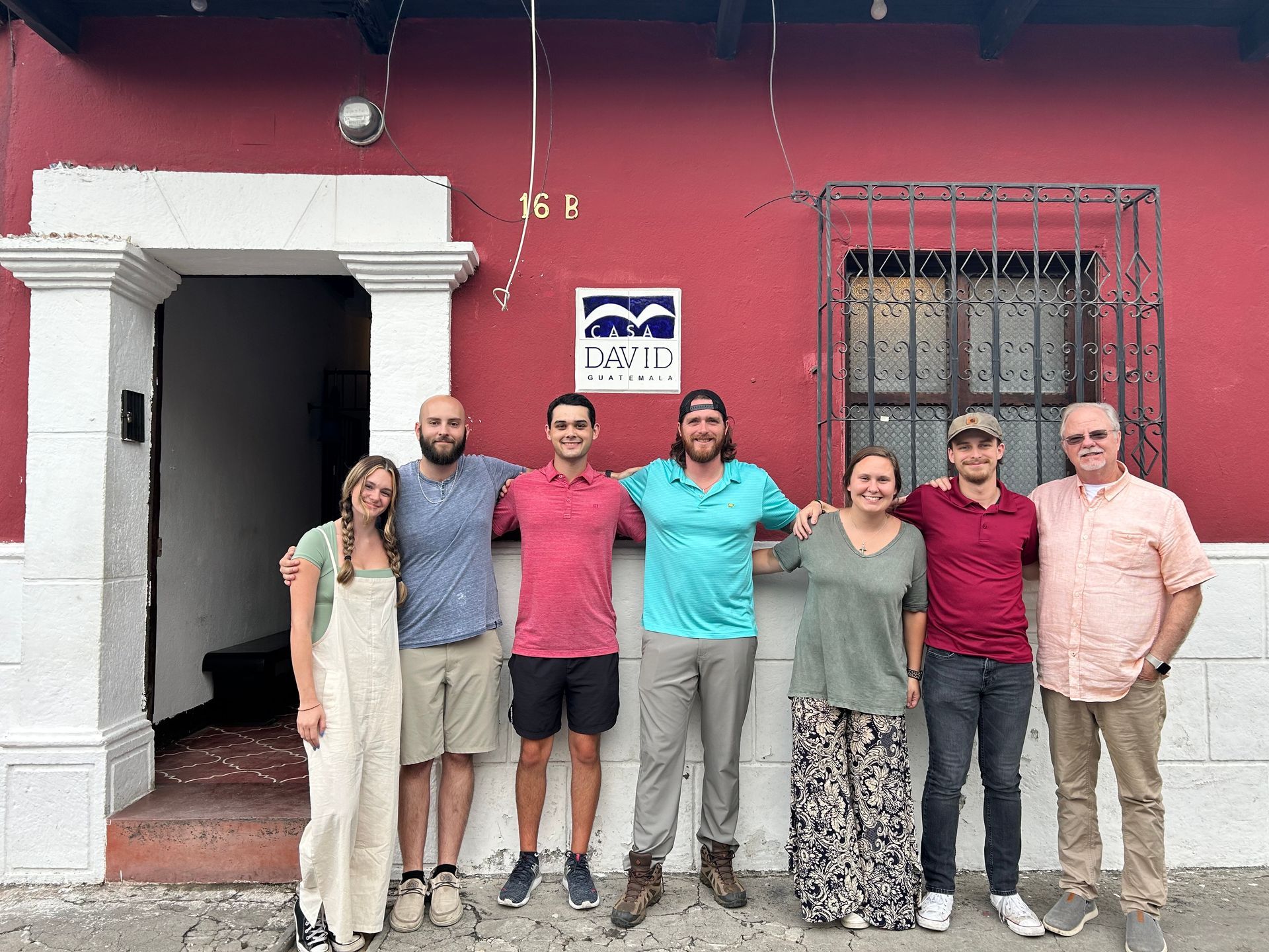 A group of 7 people are posing for a picture in front of a red building in Guatemala.