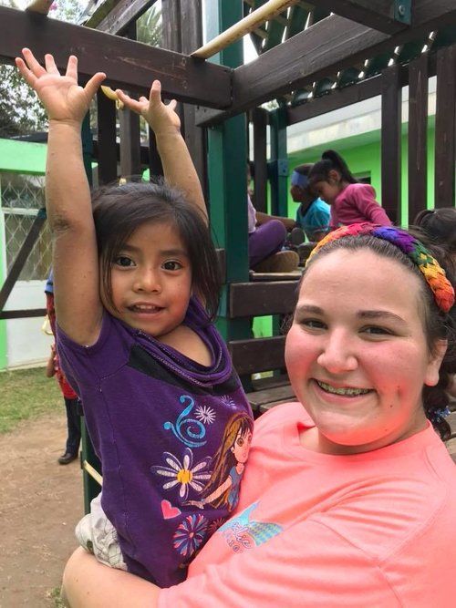 A woman in a pink shirt is holding a little girl in her arms.