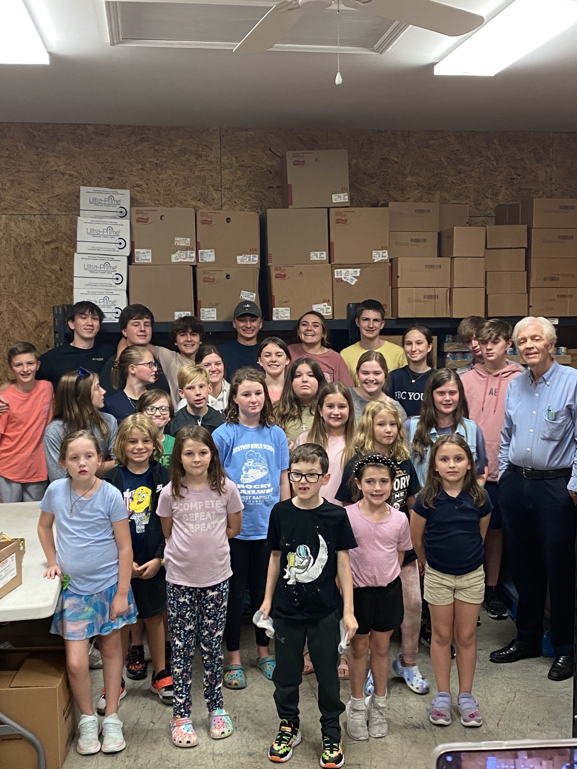 A group of young children and leaders are posing for a picture in a room with cardboard boxes behind them.
