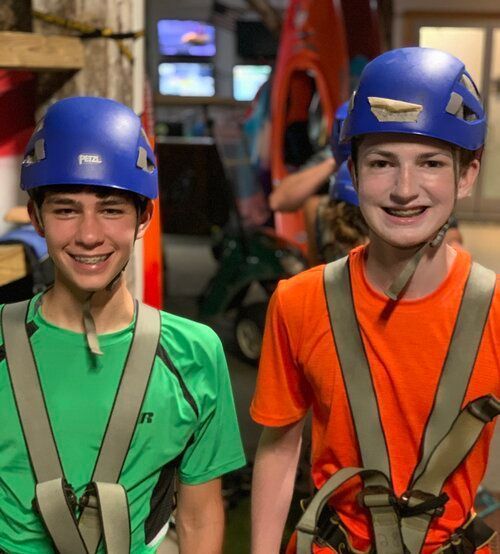 Two boys wearing helmets and harnesses are posing for a picture