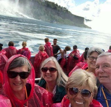 A group of people are taking a selfie on a boat in front of a waterfall.