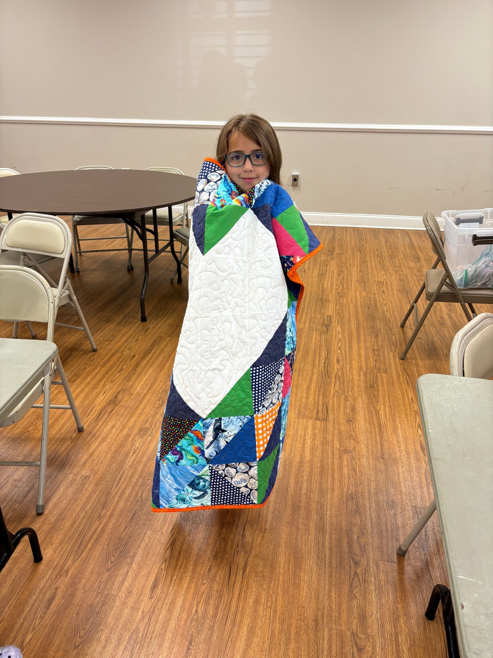 A young girl is standing with a quilt wrapped around herself.