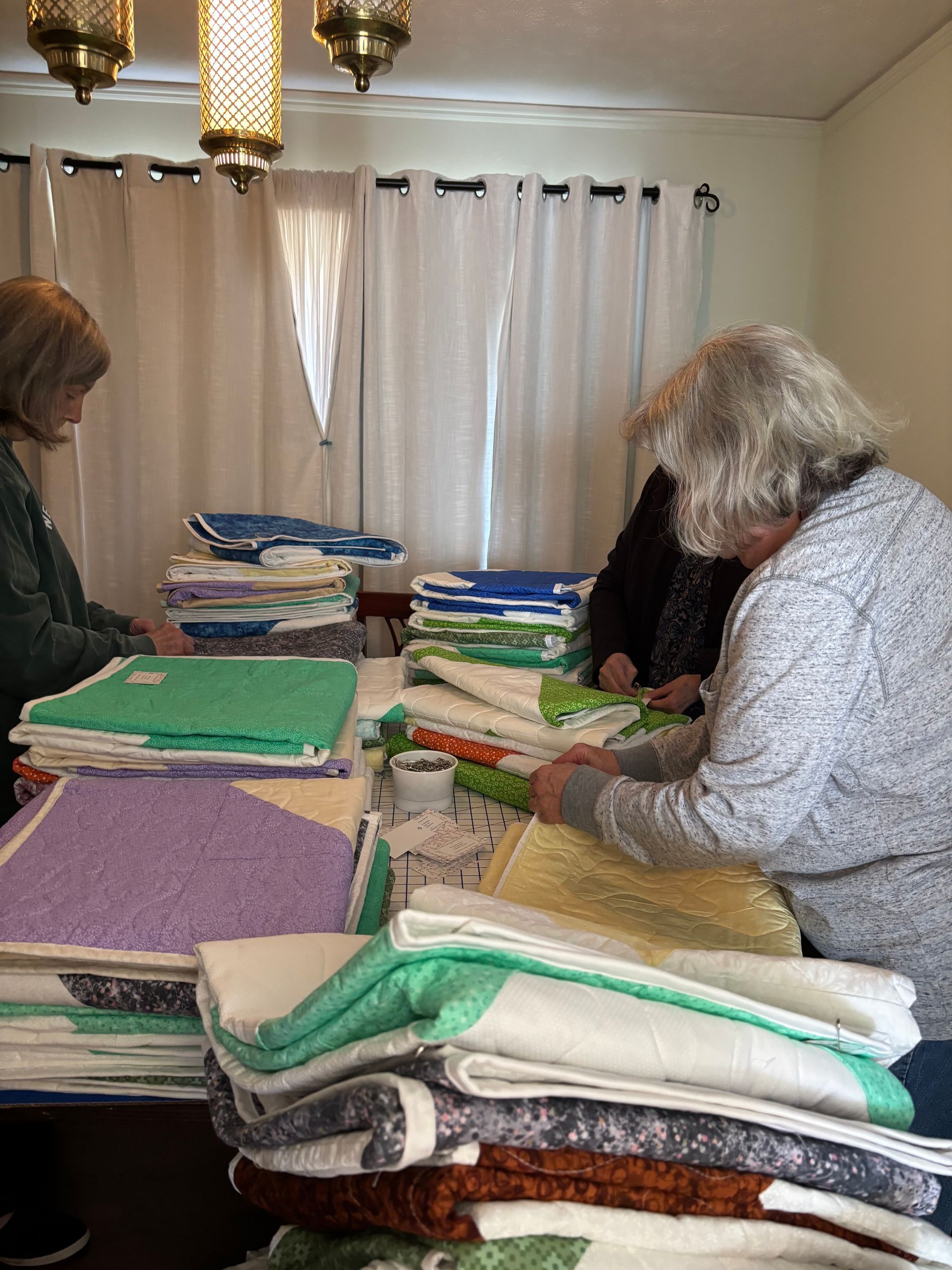 A group of women are gathered around a table working on a quilt.