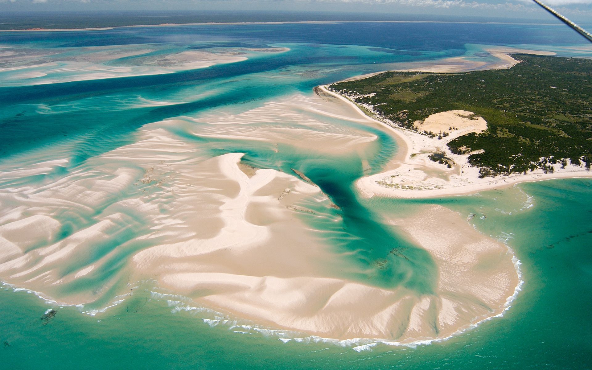 Aerial view of turquoise ocean with sandy islands and green foliage.