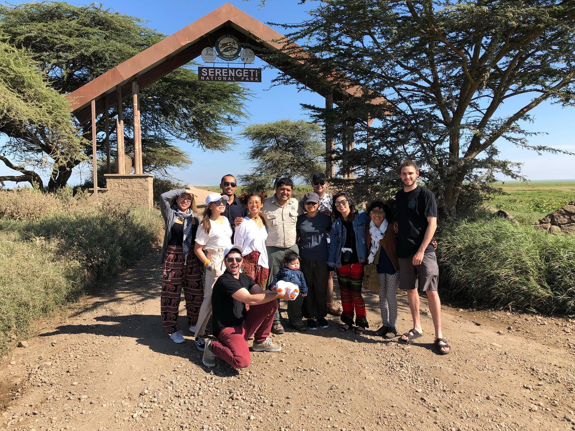 Group of people posing in front of a park entrance sign in a sunny outdoor setting.