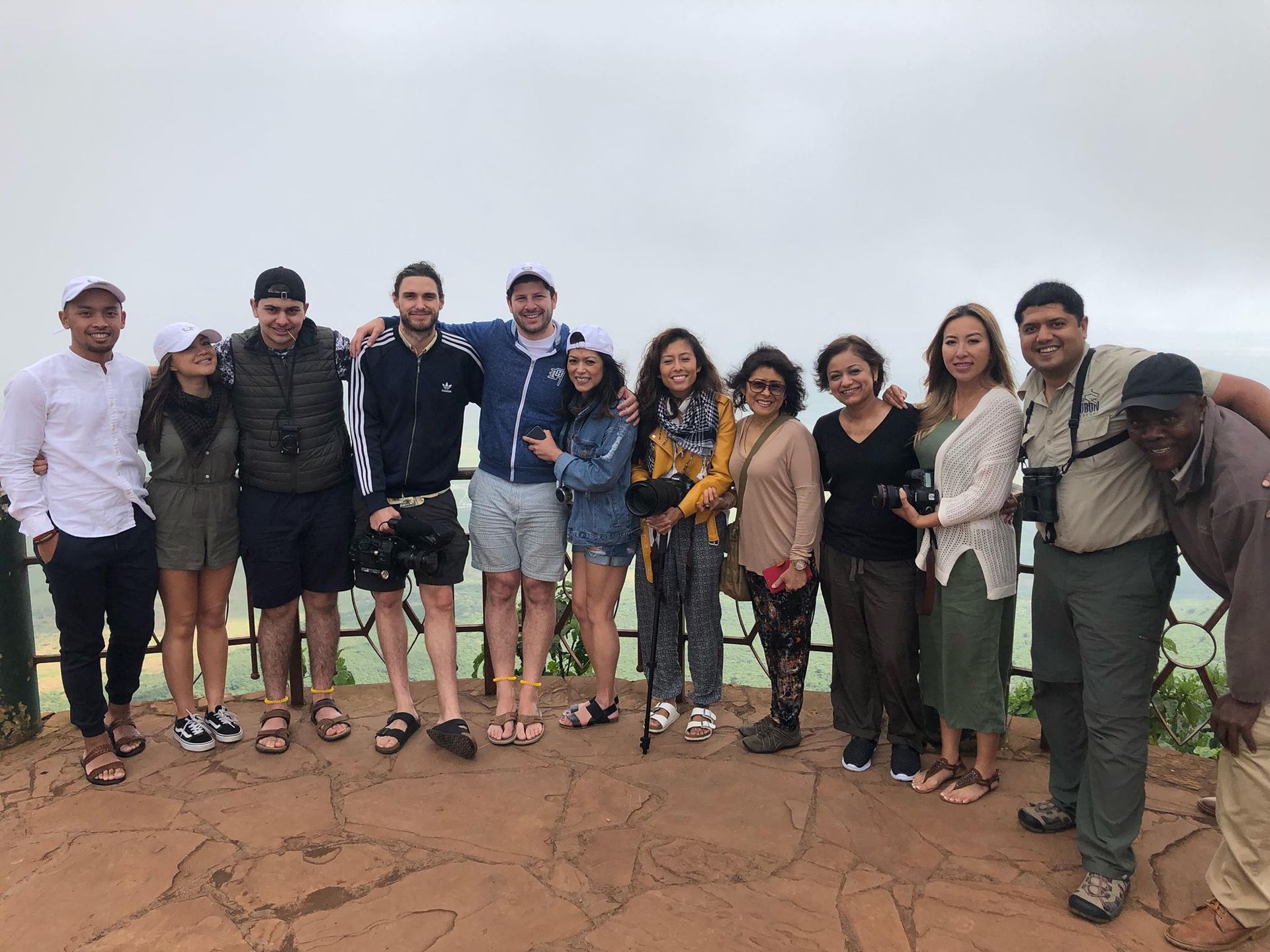 Group of people pose together outdoors on a scenic overlook. Cloudy day.