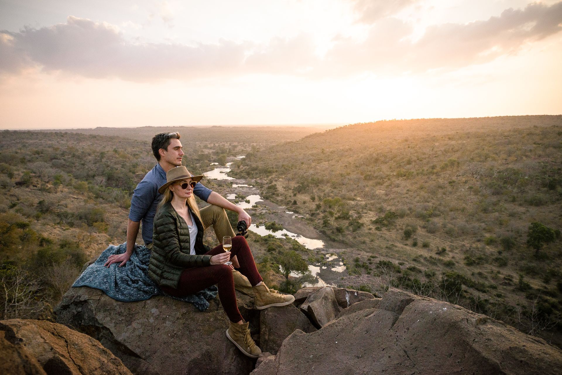 Couple sitting on a rock overlooking a river valley at sunset.
