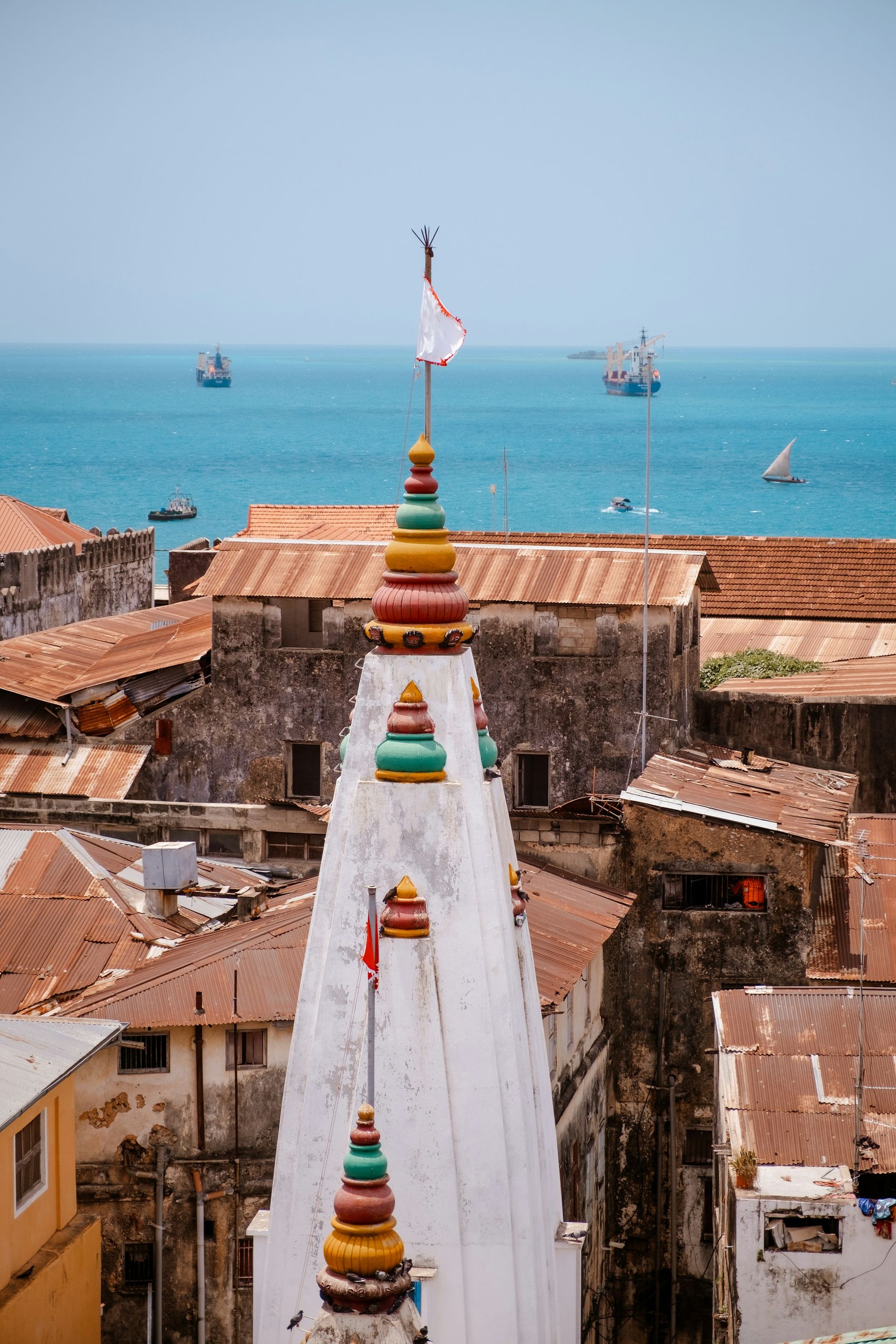 White temple spire with colorful accents, overlooking a town and the ocean with boats.